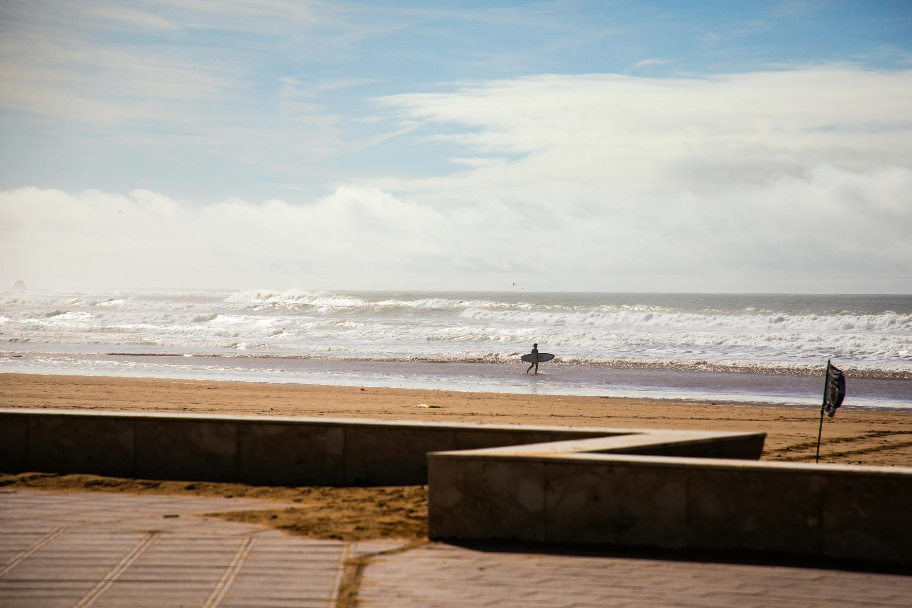 Agadir czy Taghazout? Gdzie lepiej na plażę, surfing i spokojny urlop Samotny surfer idzie po słonecznej plaży w Maroku