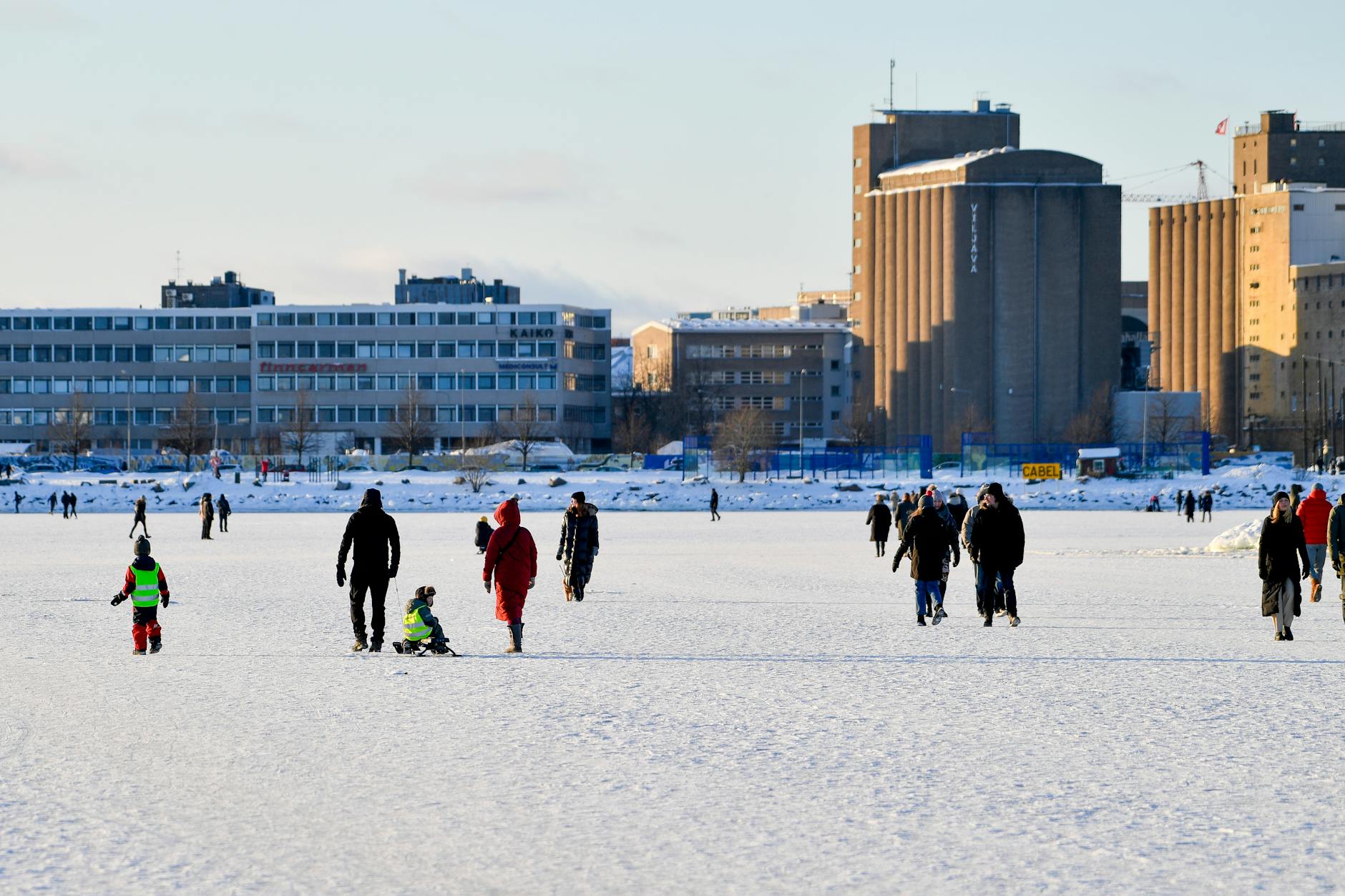 Ludzie spacerują po zamarzniętym morzu z zabudowaniami Helsinek w tle