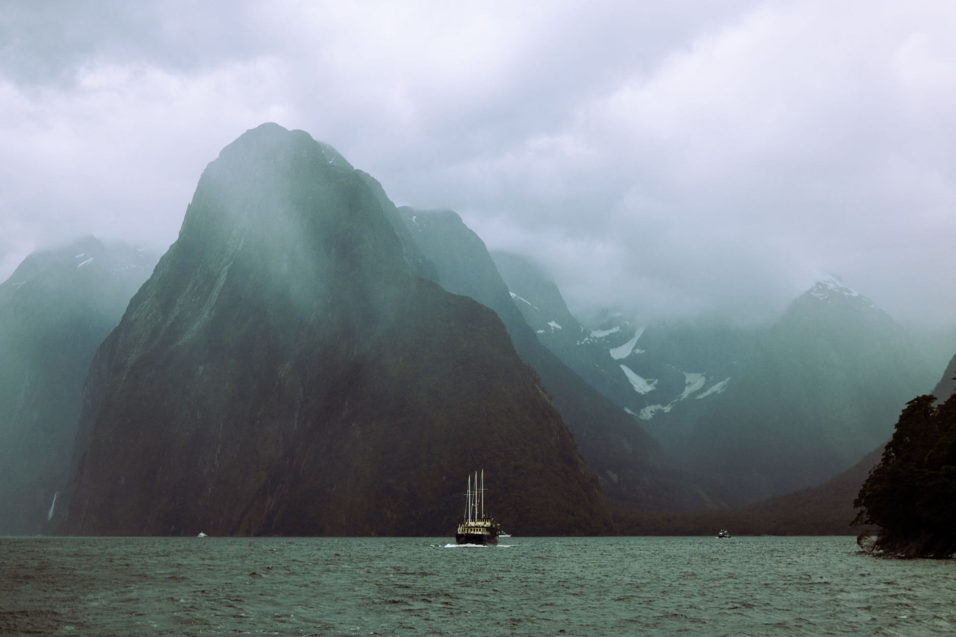 Żaglówka płynie wśród stromych, pochmurnych klifów Milford Sound